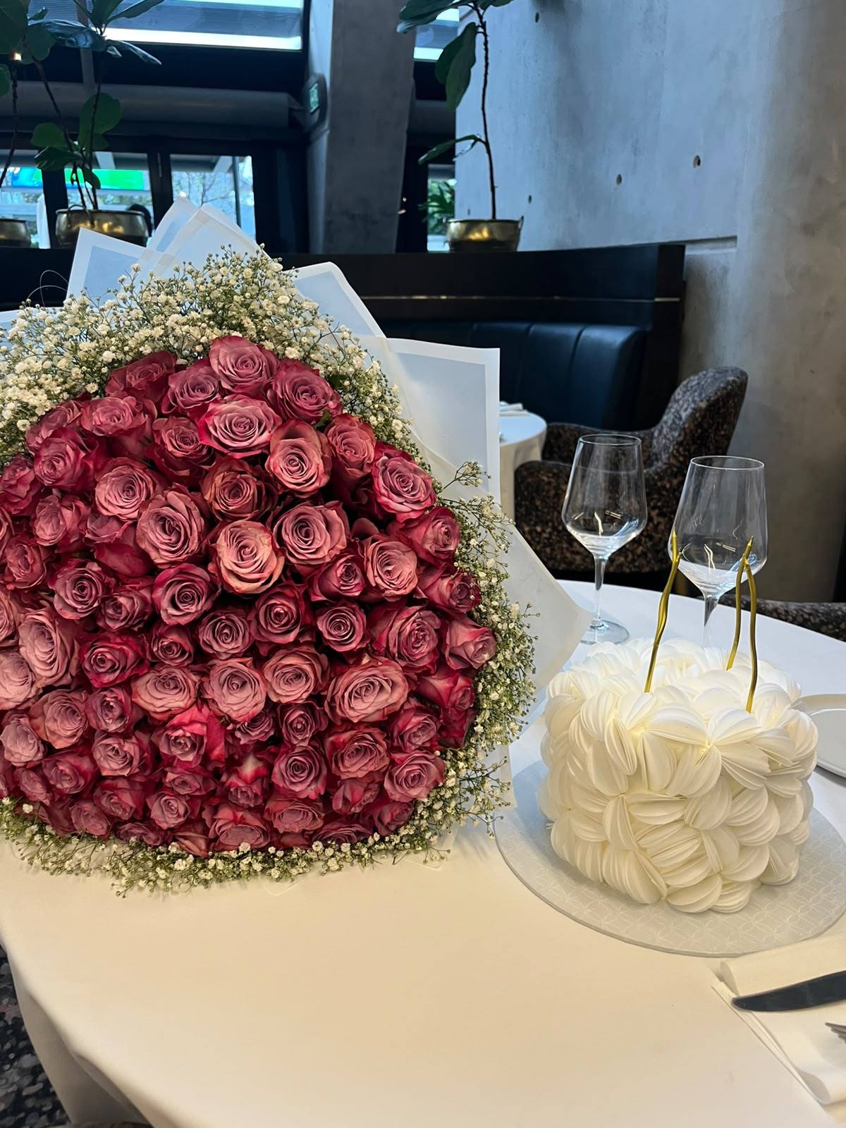 White wafer-paper signature cake beside a bouquet of pink roses